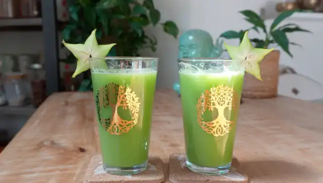 Deux verres de jus vert décorés d'un arbre de vie doré, garnis d'une tranche de carambole.