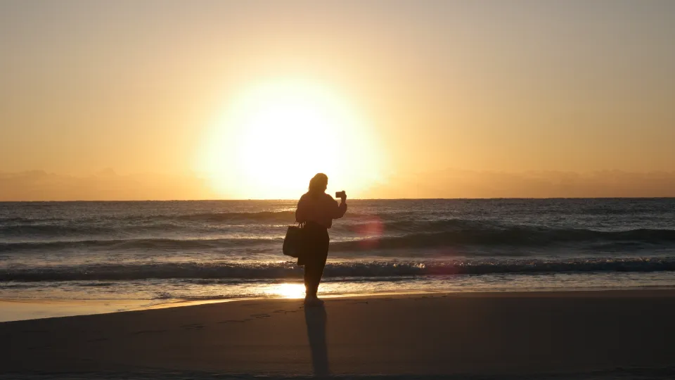 Une femme silhouette prend une photo avec son téléphone portable sur une plage au coucher du soleil.