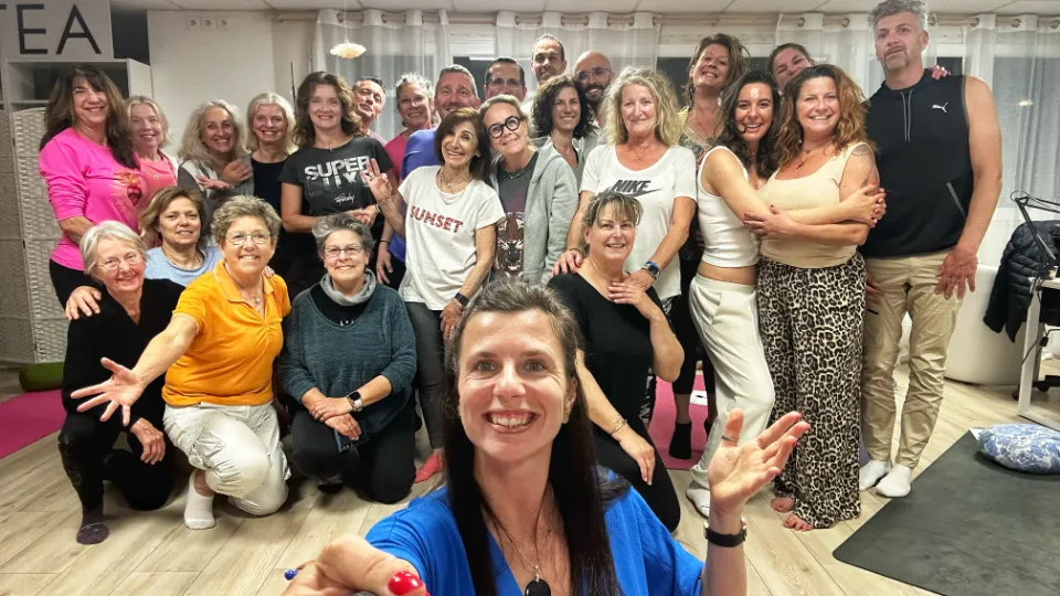 Groupe diversifié de personnes souriantes, certaines se tenant les unes aux autres, apparemment à la fin d'un cours de fitness ou de yoga.