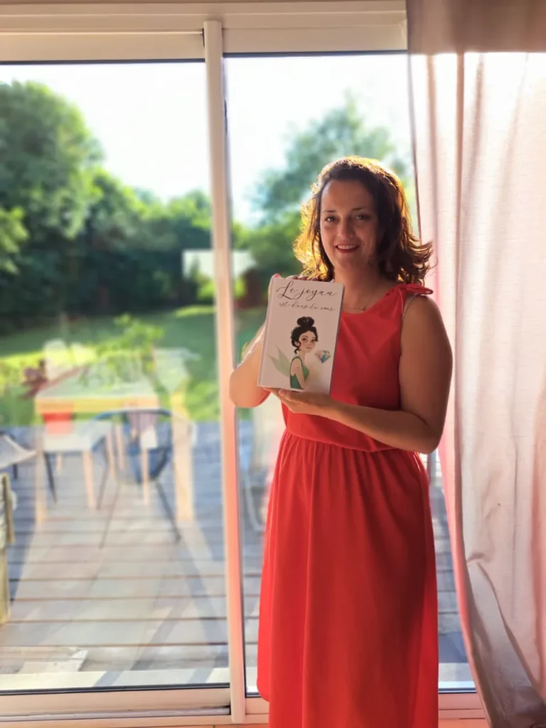 Une femme souriante en robe rouge tient le livre "Le Joyau" qui représente une femme à la coiffure relevée et un diamant.