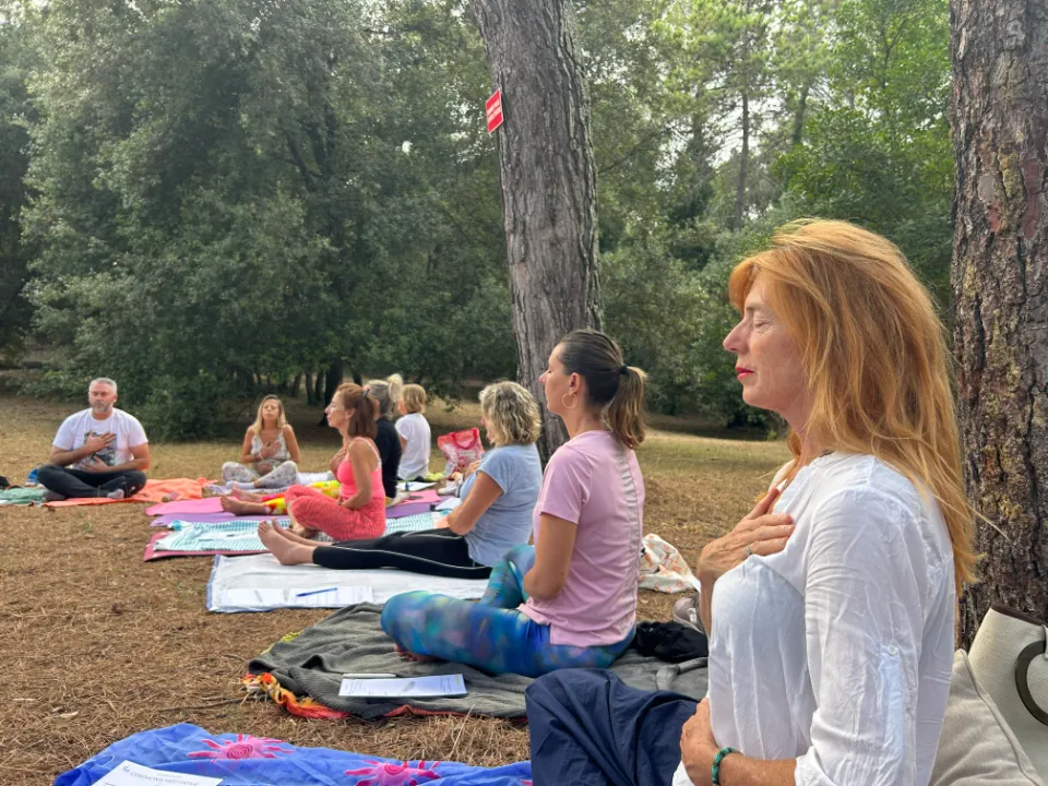 Un groupe de personnes participe à une séance de yoga et de méditation en plein air, assis sur des tapis au milieu des arbres.