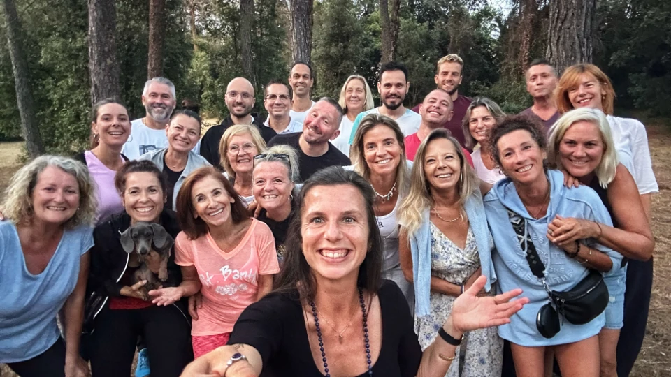 Groupe souriant de personnes, hommes et femmes, posant pour une photo en extérieur avec des arbres en arrière-plan et un chien.