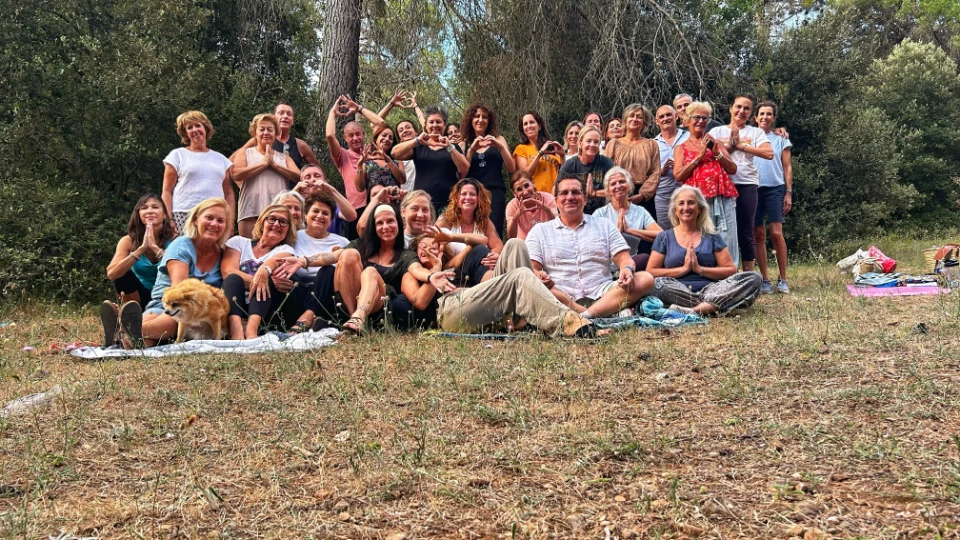Un groupe diversifié de personnes assises et allongées sur une couverture dans un pré, certaines faisant des gestes de cœur avec leurs mains.